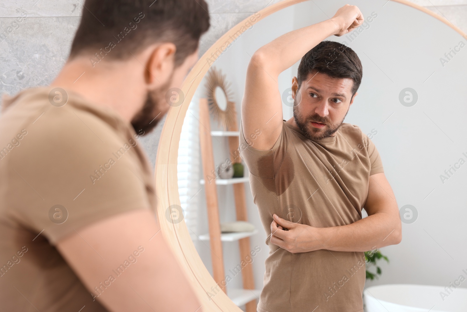 Photo of Emotional man in t-shirt before using deodorant near mirror at home