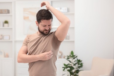 Emotional man in t-shirt before using deodorant at home. Space for text