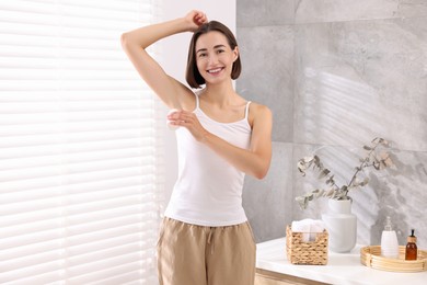 Photo of Smiling woman applying roll-on deodorant at home