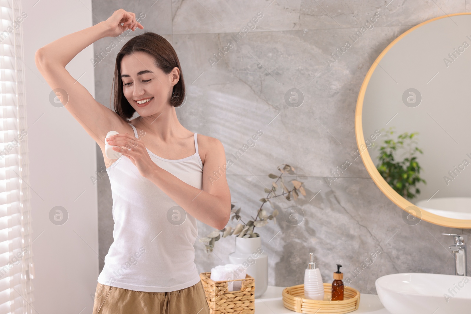 Photo of Smiling woman applying roll-on deodorant at home