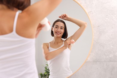 Photo of Smiling woman applying roll-on deodorant near mirror at home