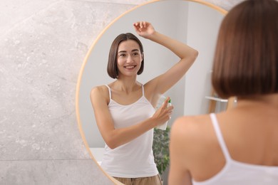 Photo of Smiling woman applying spray deodorant near mirror at home. Space for text