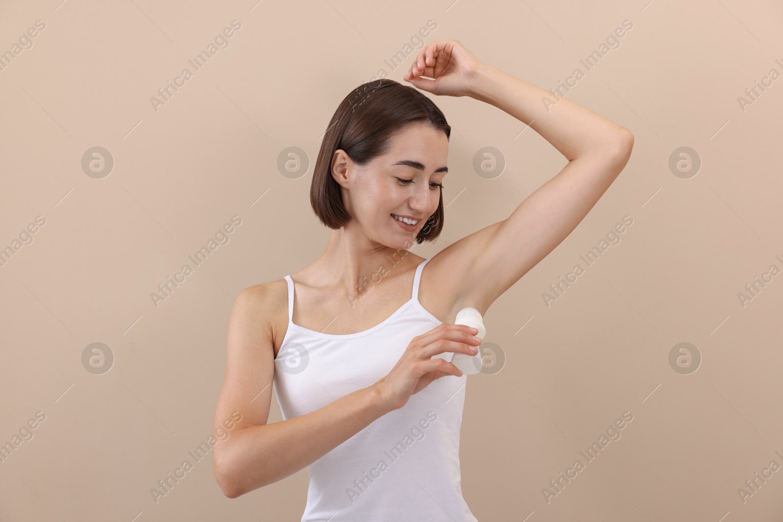 Photo of Smiling woman applying roll-on deodorant on beige background