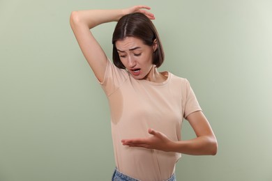 Emotional woman in t-shirt before using deodorant on green background