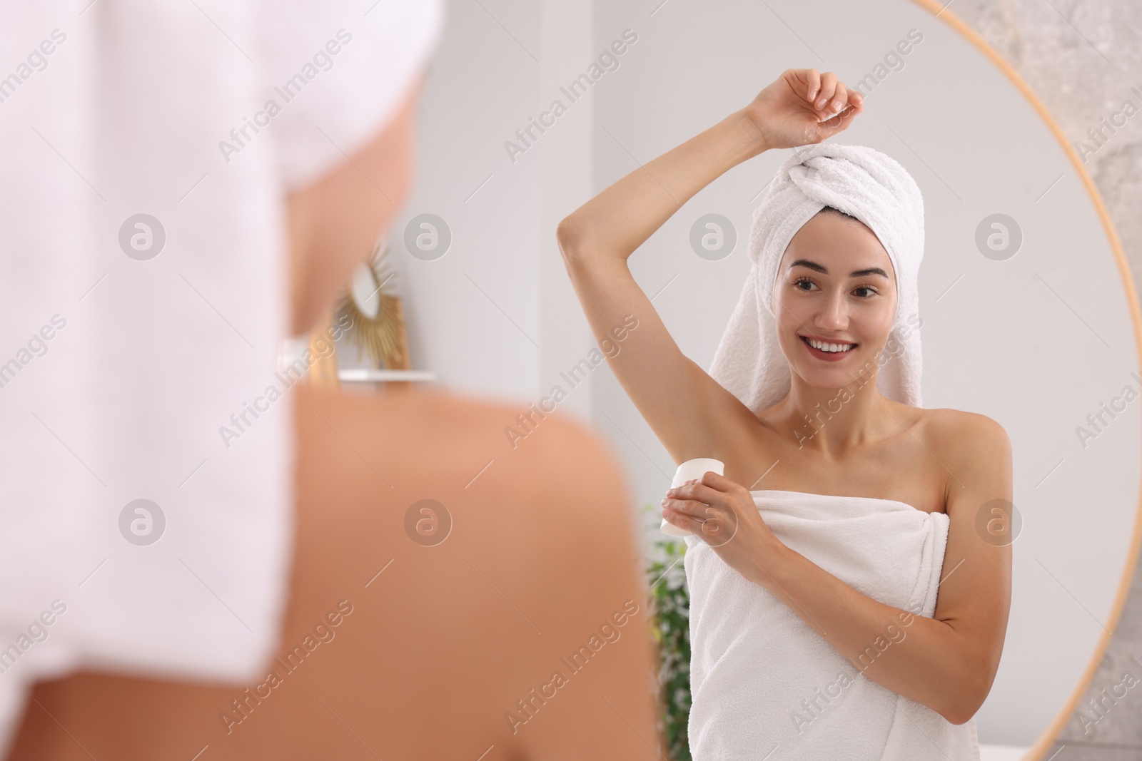 Photo of Smiling woman applying solid deodorant near mirror at home