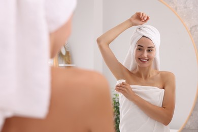 Photo of Smiling woman applying solid deodorant near mirror at home