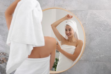 Photo of Smiling woman applying spray deodorant near mirror at home, back view