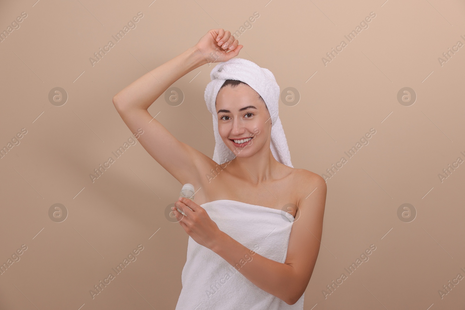 Photo of Smiling woman applying roll-on deodorant on beige background