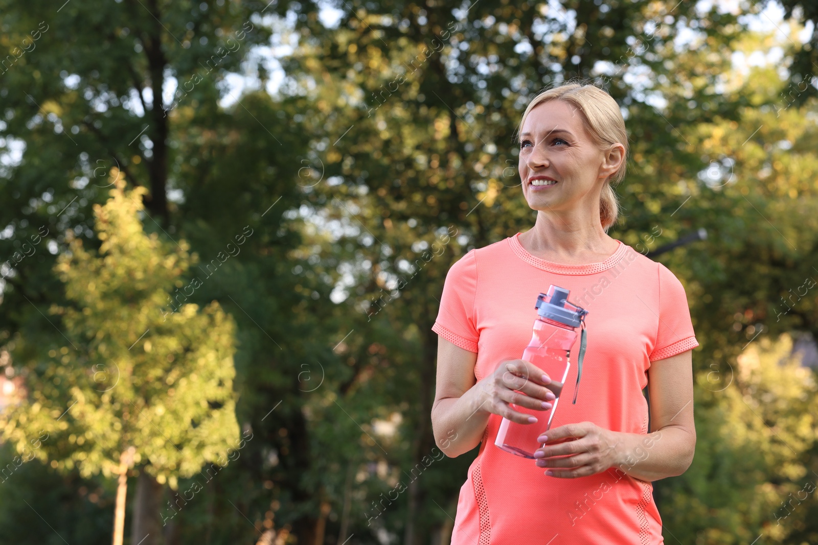 Photo of Happy woman with bottle of water in park, space for text