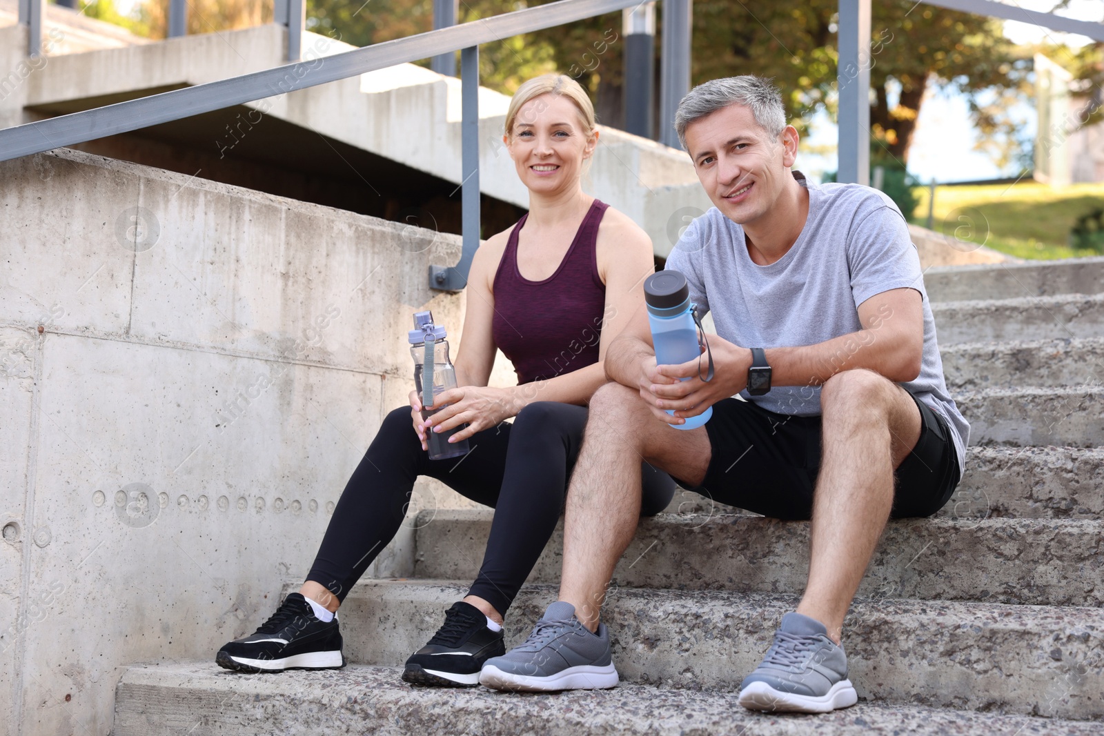 Photo of Smiling couple with bottles of water on steps outdoors