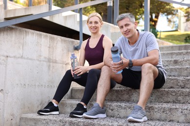 Photo of Smiling couple with bottles of water on steps outdoors