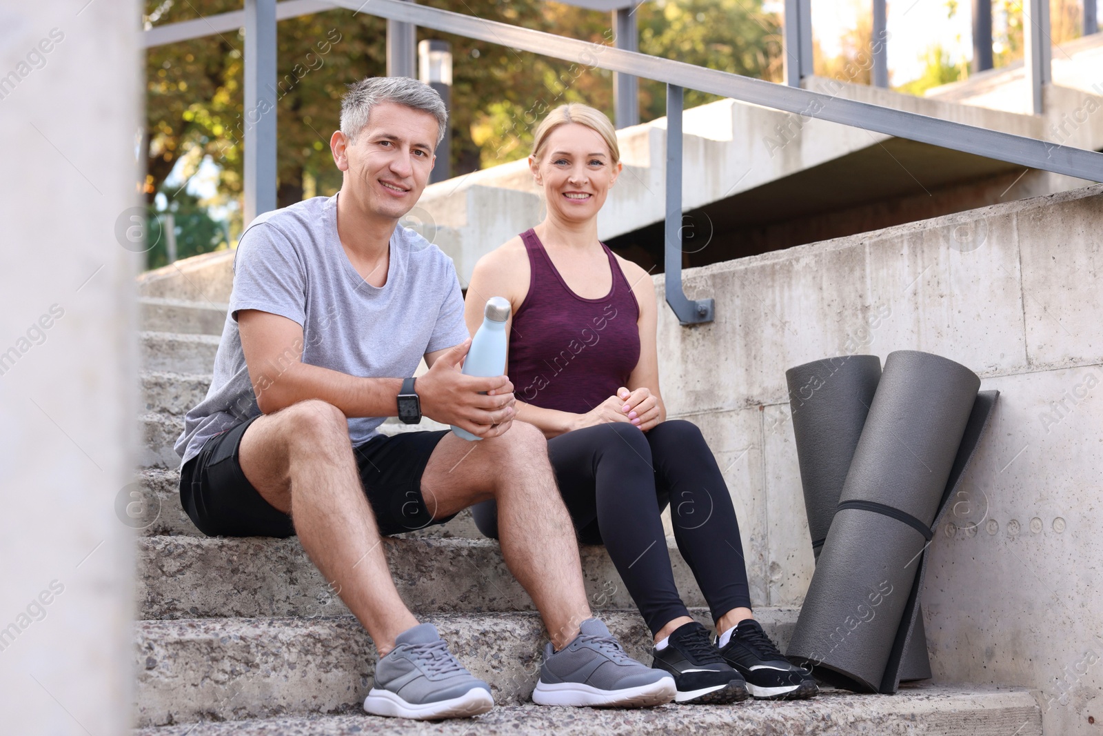 Photo of Smiling couple with bottle of water and mats on steps outdoors