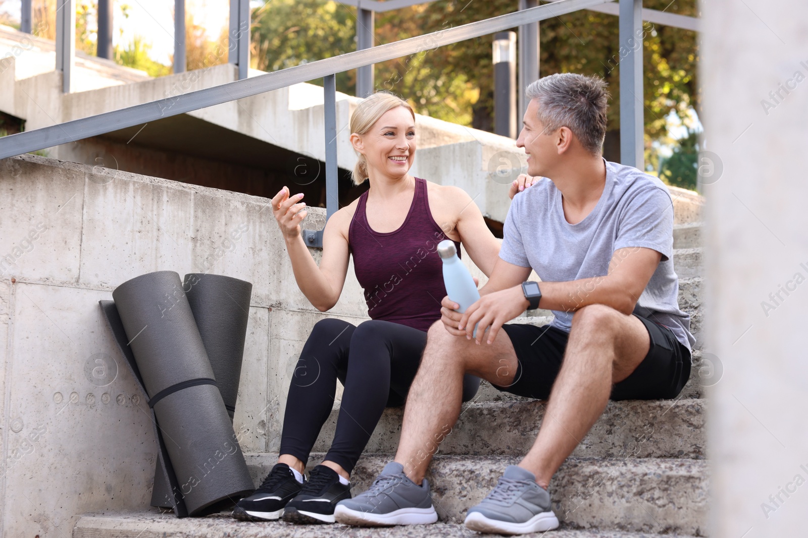 Photo of Smiling couple with bottle of water and mats on steps outdoors