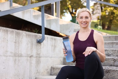 Photo of Smiling woman with bottle of water on steps outdoors