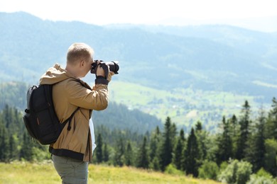 Photo of Photographer with backpack and camera taking picture of beautiful mountains. Space for text