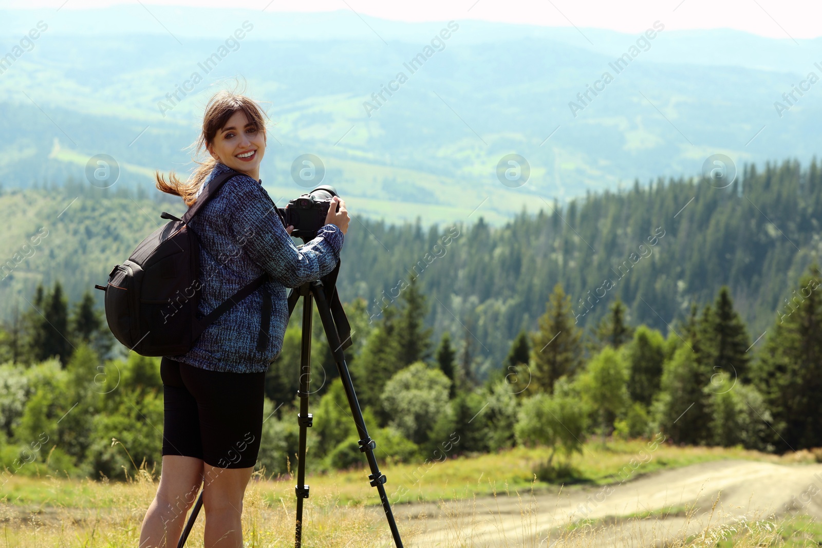 Photo of Photographer with backpack and camera on tripod taking picture of beautiful mountains. Space for text