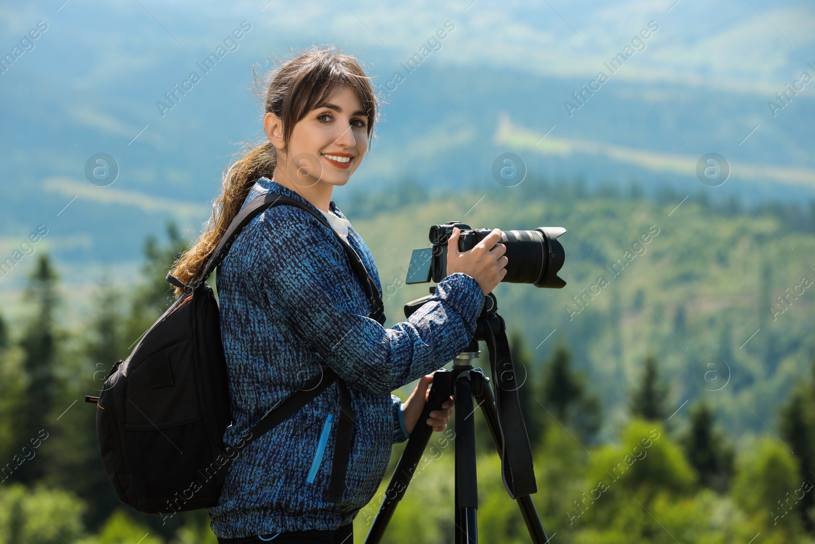 Photo of Photographer with backpack and camera on tripod taking picture of beautiful mountains