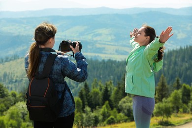 Photo of Photographer with backpack and camera taking picture of model in beautiful mountains