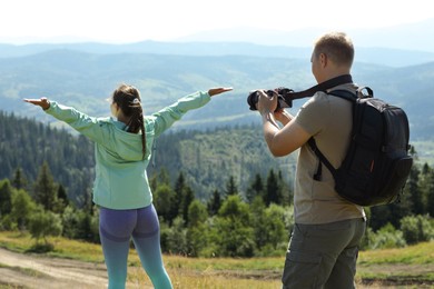 Photo of Photographer with backpack and camera taking picture of model in beautiful mountains