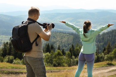 Photo of Photographer with backpack and camera taking picture of model in beautiful mountains