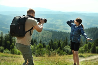 Photo of Photographer with backpack and camera taking picture of model in beautiful mountains