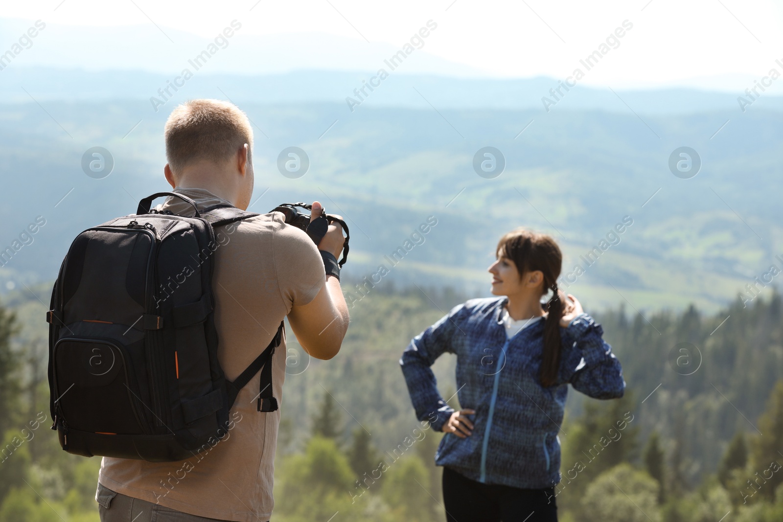 Photo of Photographer with backpack and camera taking picture of model in beautiful mountains, back view