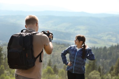 Photographer with backpack and camera taking picture of model in beautiful mountains, back view