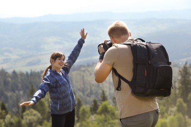 Photographer with backpack and camera taking picture of model in beautiful mountains, back view