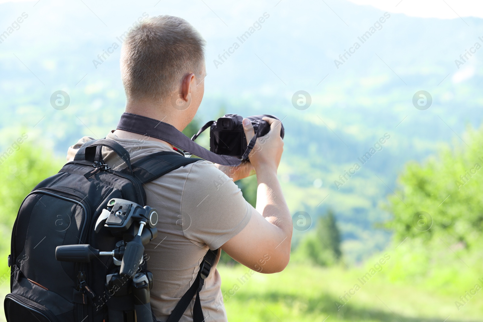 Photo of Photographer with backpack and camera taking picture of beautiful mountains, back view