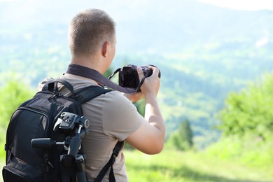 Photo of Photographer with backpack and camera taking picture of beautiful mountains, back view