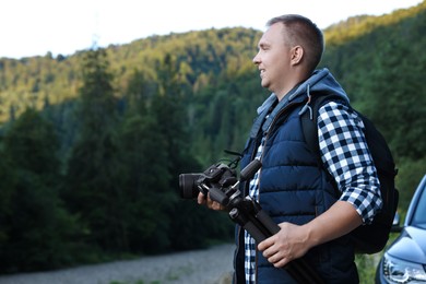 Photo of Photographer with backpack, tripod and camera in beautiful mountains. Space for text