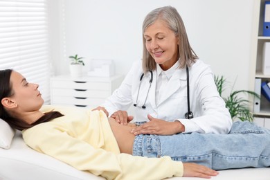 Photo of Doctor examining woman with stomach pain on couch in clinic