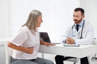 Photo of Doctor consulting senior patient with stomach pain at table in clinic