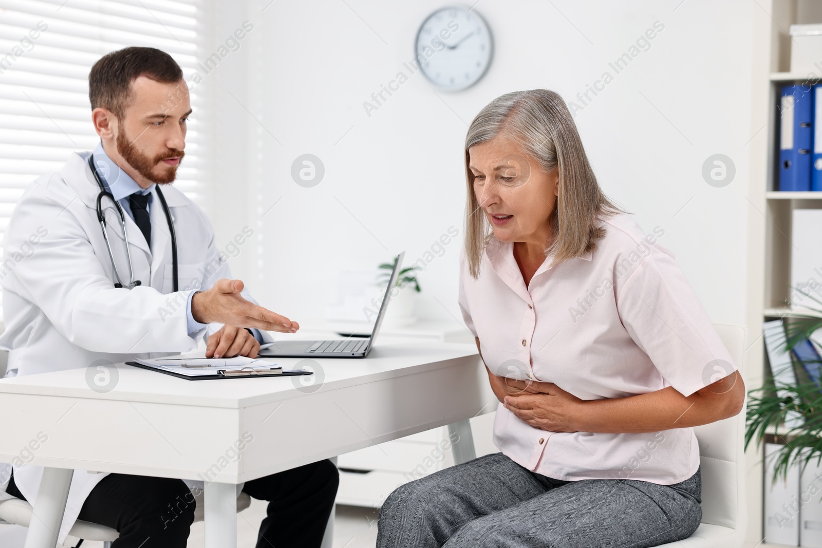 Photo of Doctor consulting senior patient with stomach pain at table in clinic