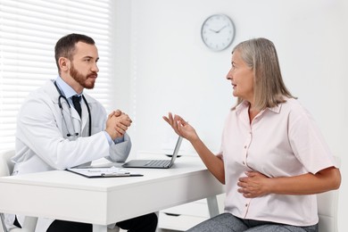 Photo of Doctor consulting senior patient with stomach pain at table in clinic