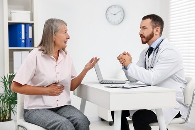 Photo of Doctor consulting senior patient with stomach pain at table in clinic