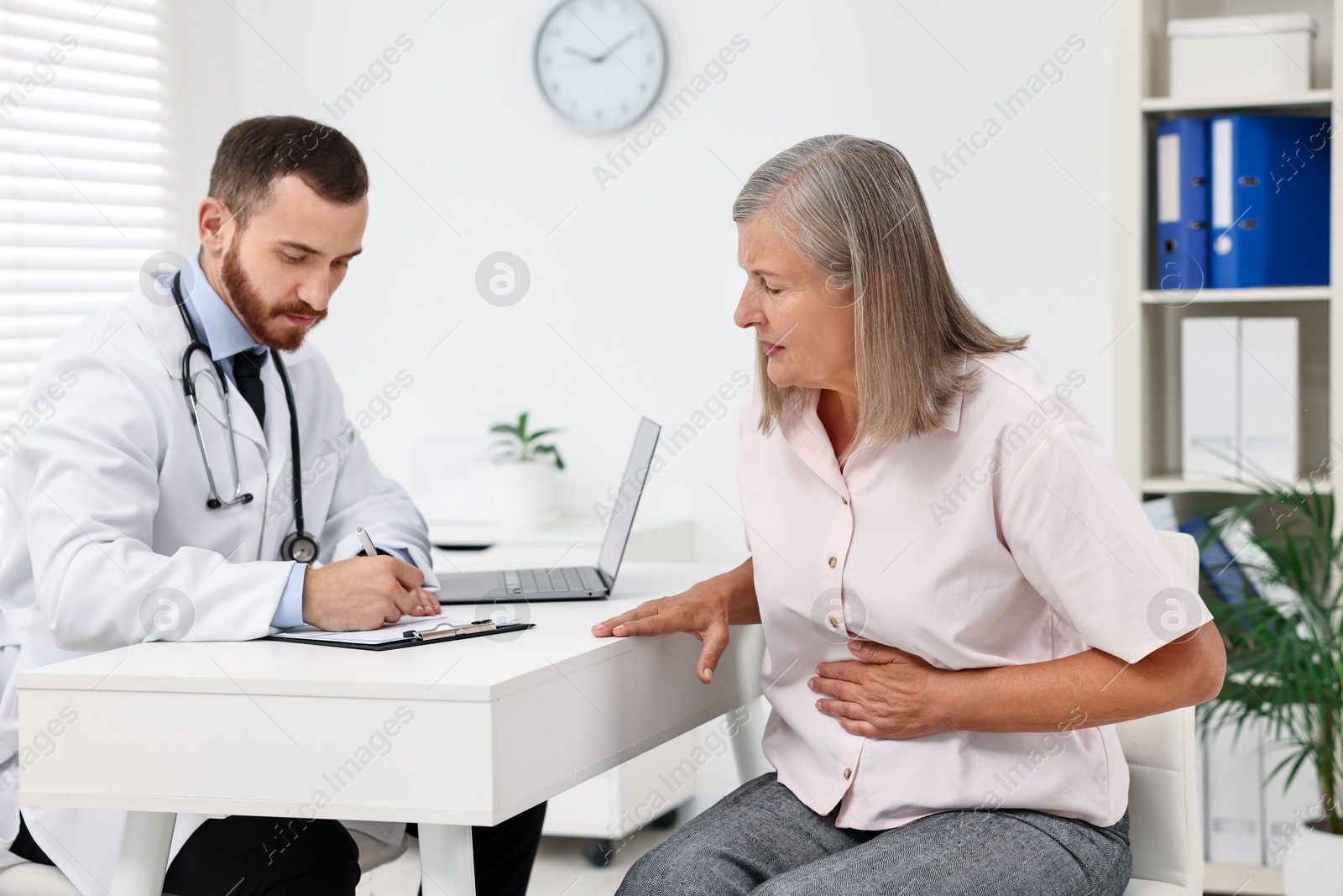 Photo of Doctor consulting senior patient with stomach pain at table in clinic