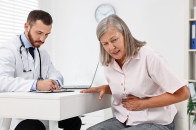 Photo of Doctor consulting senior patient with stomach pain at table in clinic