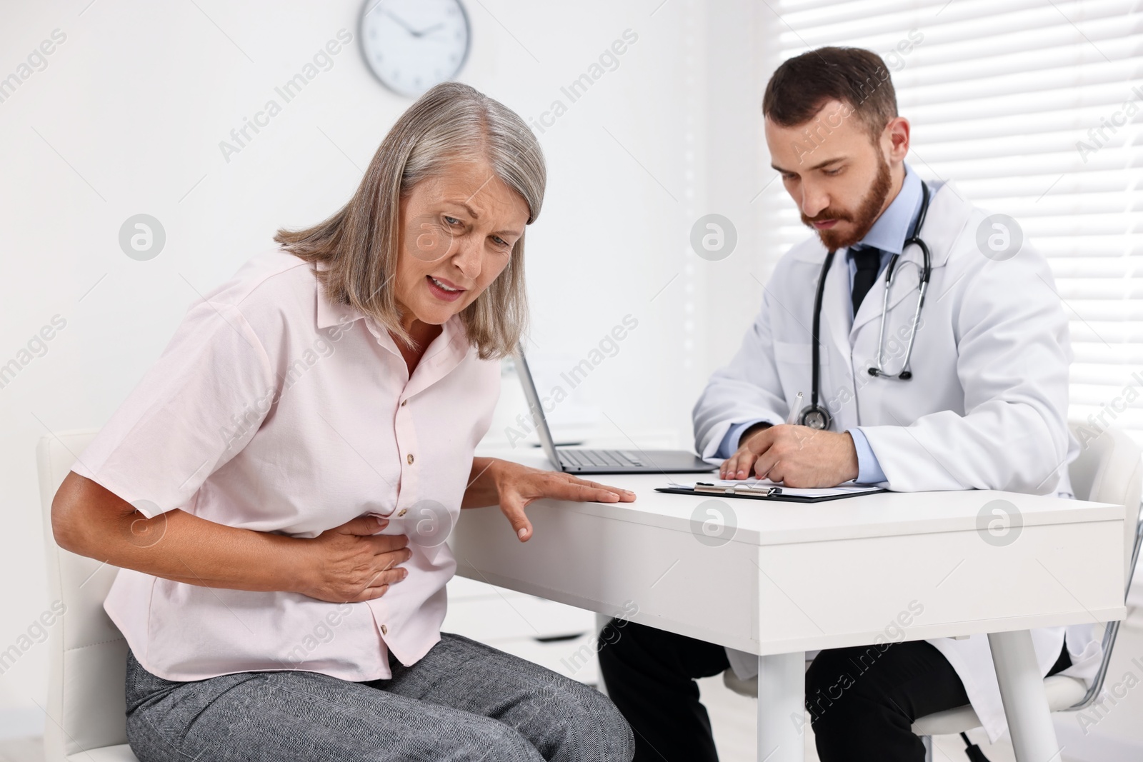 Photo of Doctor consulting senior patient with stomach pain at table in clinic