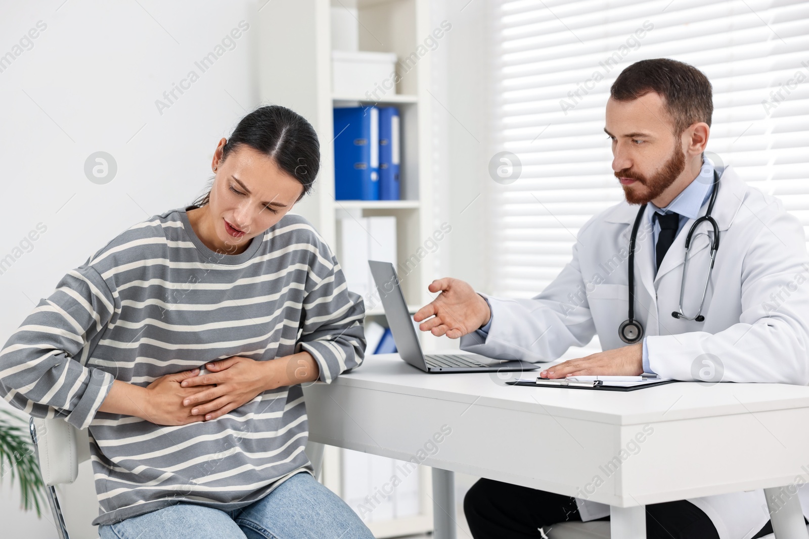 Photo of Doctor consulting patient with stomach pain at table in hospital