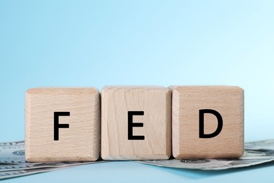 Photo of Wooden cubes with letters Fed (Federal Reserve System) and dollar banknotes on light blue background, closeup