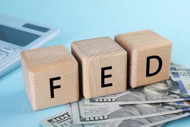 Photo of Wooden cubes with letters Fed (Federal Reserve System) and dollar banknotes on light blue background, closeup