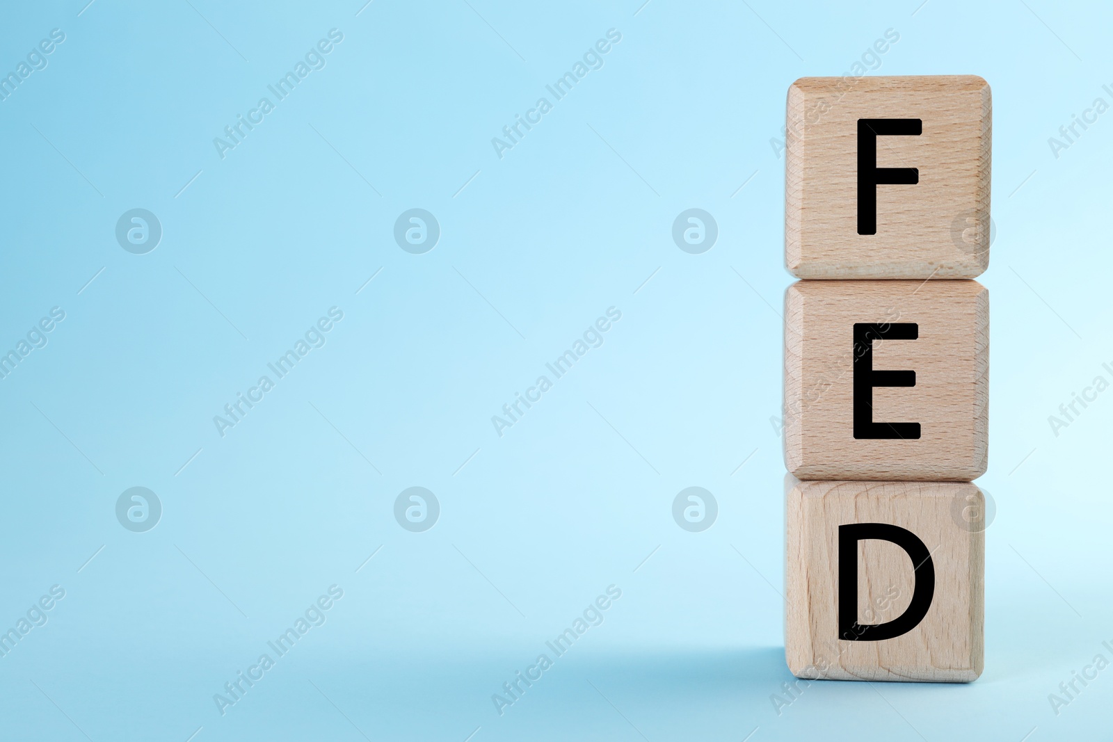 Photo of Stack of wooden cubes with letters Fed (Federal Reserve System) on light blue background, closeup. Space for text