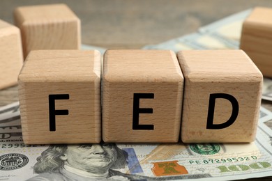 Photo of Wooden cubes with letters Fed (Federal Reserve System) and dollar banknotes on table, closeup