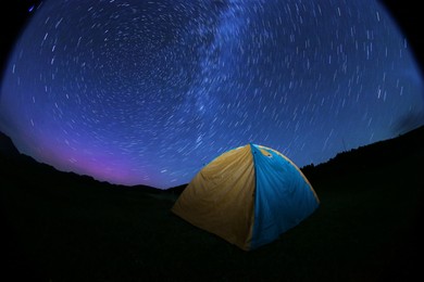 Photo of Modern camping tent in wilderness at night. Fisheye lens effect