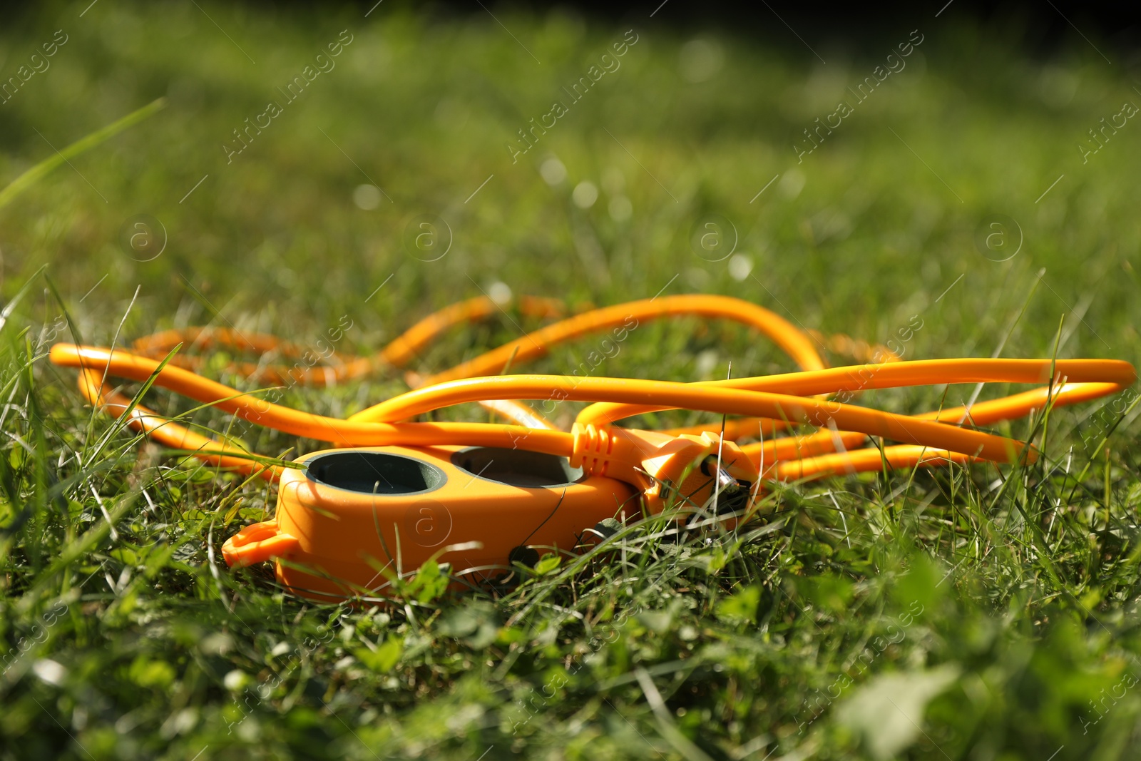 Photo of Orange extension cord on green grass outdoors, closeup