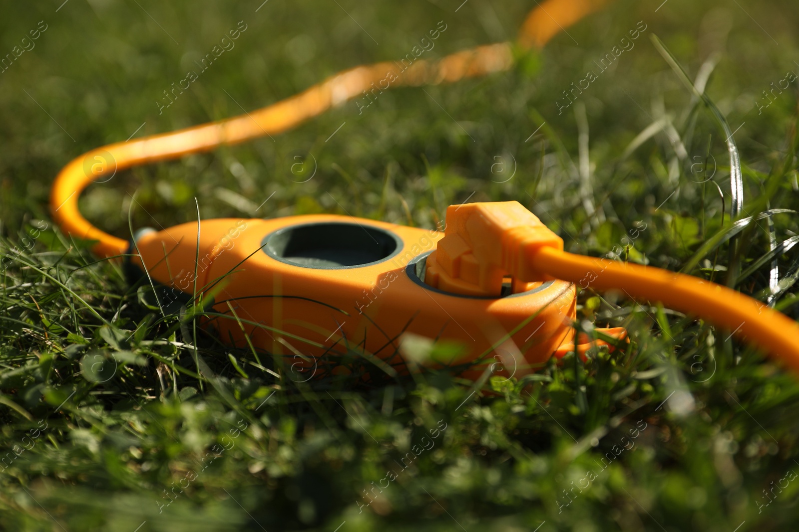 Photo of Orange extension cord on green grass outdoors, closeup