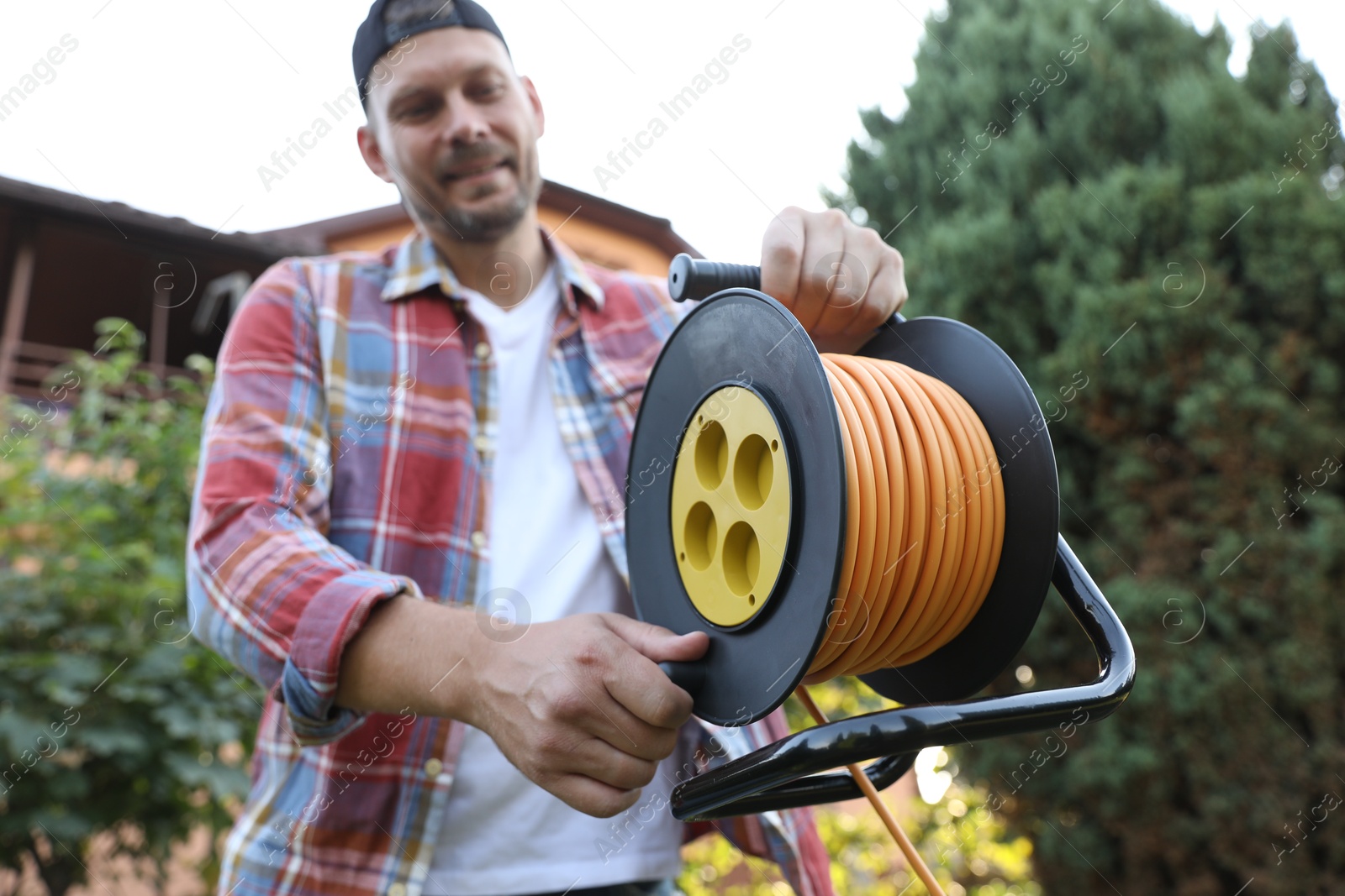 Photo of Man with extension cord reel outdoors, selective focus