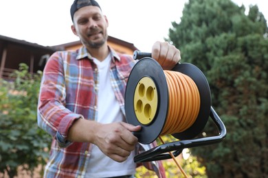 Man with extension cord reel outdoors, selective focus