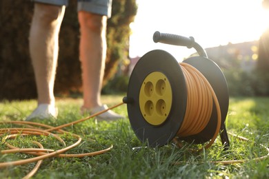 Photo of Man near extension cord reel on green grass outdoors, closeup